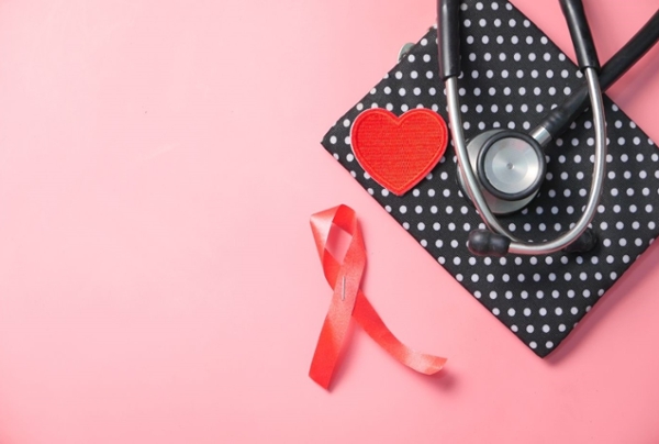 Red ribbon, booklet, and stethoscope on a pink backdrop.